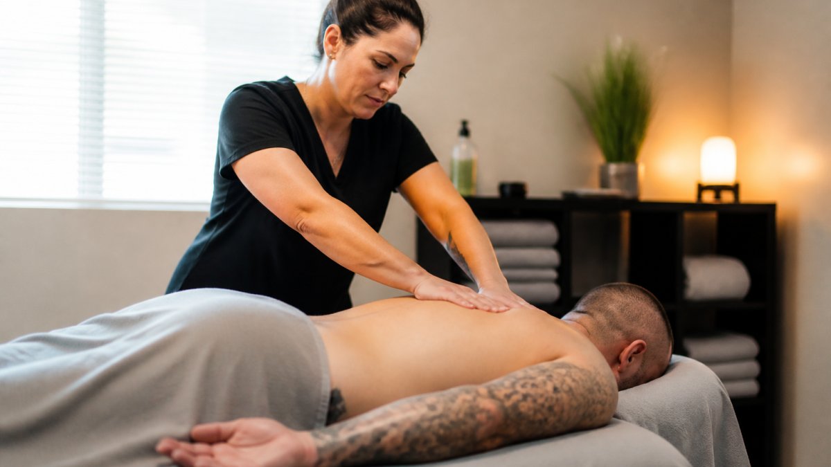 Licensed massage therapist performing therapeutic massage on veteran client in calm, professional treatment room with soft lighting and soothing atmosphere