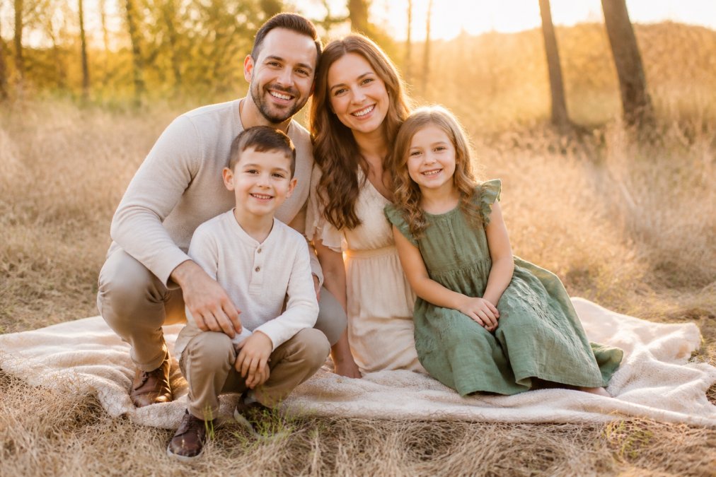 Family of four wearing coordinated neutral base outfits with complementary accent colors during outdoor portrait session in golden hour lighting, showing relaxed poses and genuine smiles