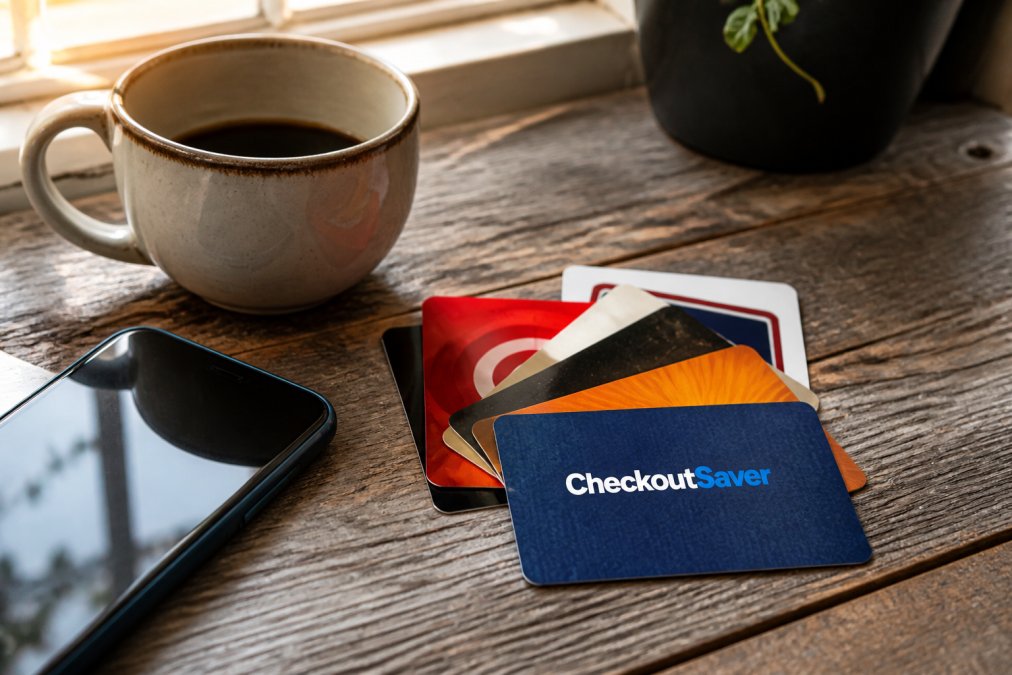 Close-up of several retail gift cards fanned out on a weathered wooden surface next to a smartphone and a ceramic mug of coffee, warm morning light from a nearby window