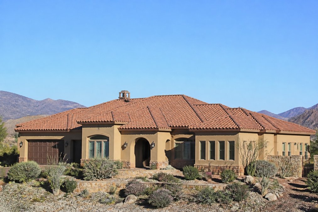 Wide shot of a Southwest-style home with a clay tile roof in a dry desert landscape, showing the full roofing system against a clear blue sky