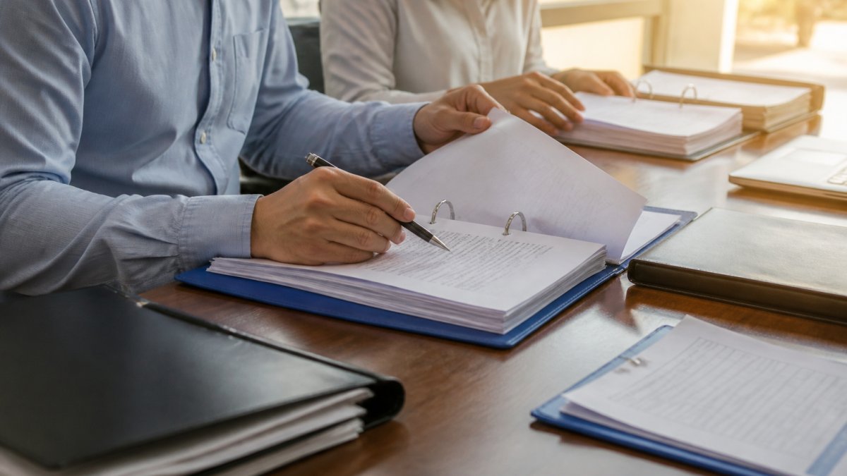 Medical device manufacturer team reviewing documentation and quality management records at a desk with binders and laptops in a regulated facility