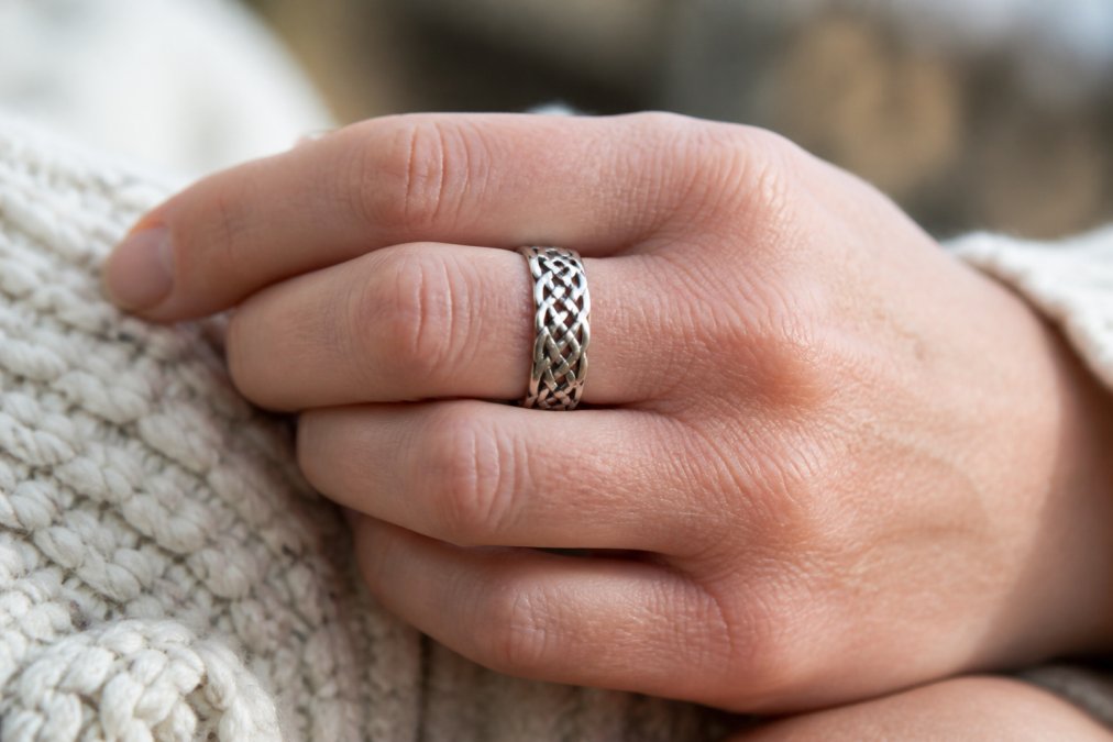 A person wearing a silver ring featuring intricate celtic knotwork in soft natural lighting.