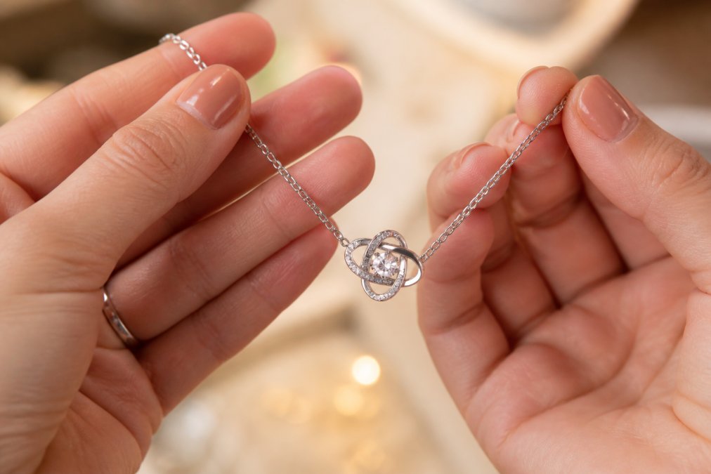 Close-up of an elegant engraved necklace with cubic zirconia crystals being held by hands, displayed against a soft blurred background with warm lighting