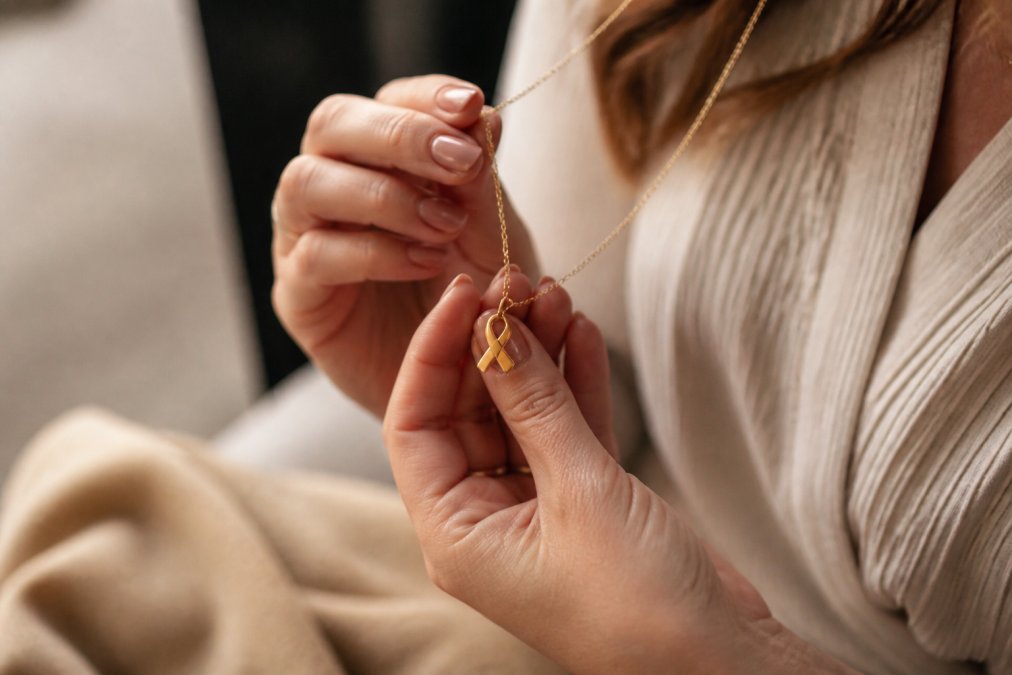 Hands holding a delicate gold ribbon necklace as one of many meaningful anniversary gifts for a couple.