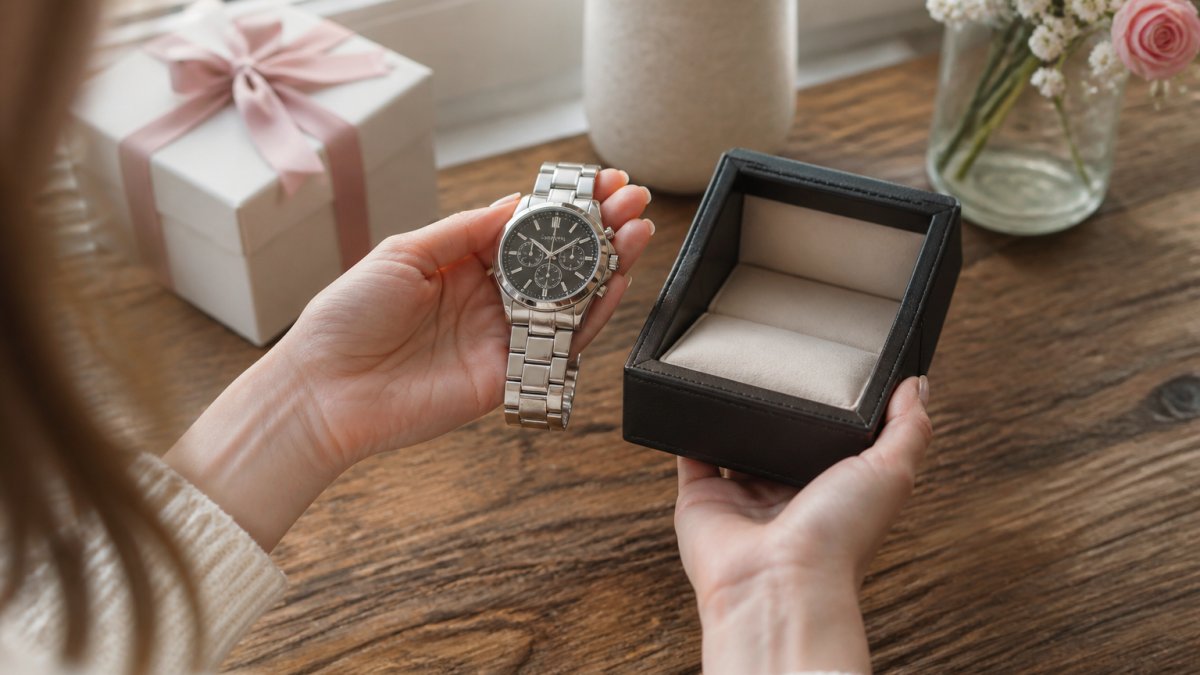 Close-up of a wife's hands holding an engraved silver watch and a small custom jewelry box, soft natural window light, warm and intimate setting on a wooden table