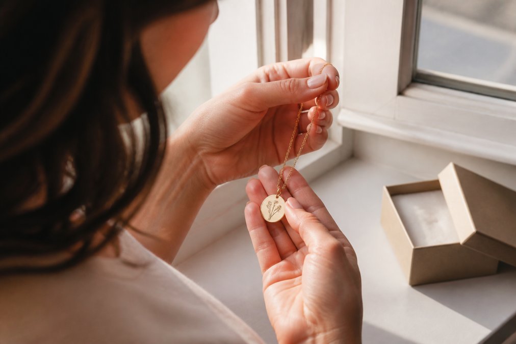 Woman holding a delicate gold pendant necklace as one of the most meaningful anniversary gifts for her