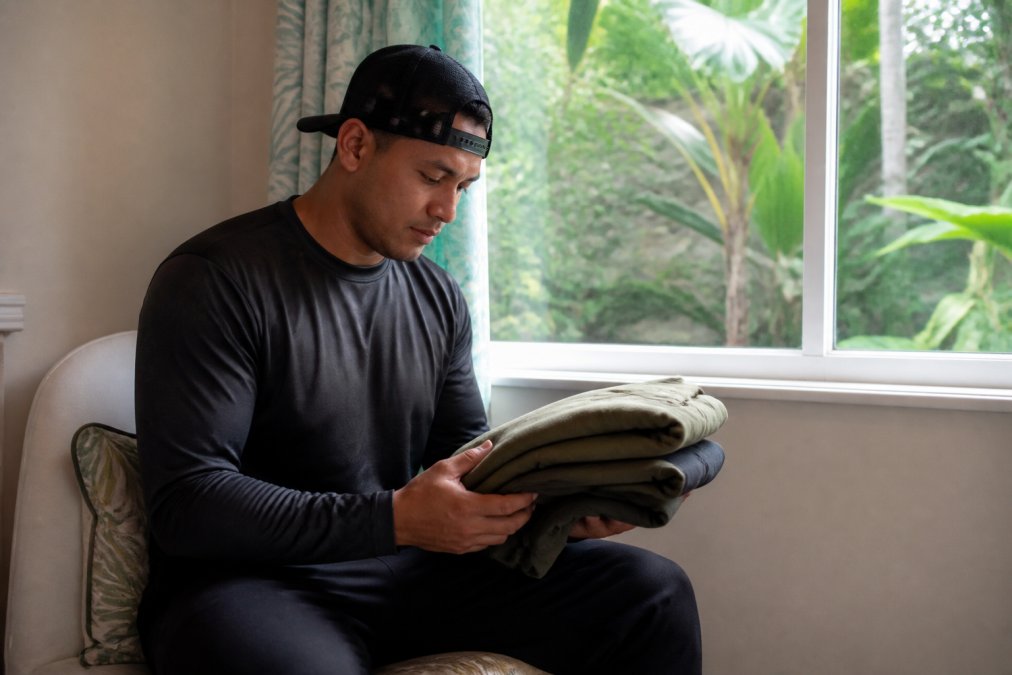 Person sitting by a window with natural light, hands holding folded meaningful apparel, thoughtfully reading the message while reflecting on personal values and intentional living