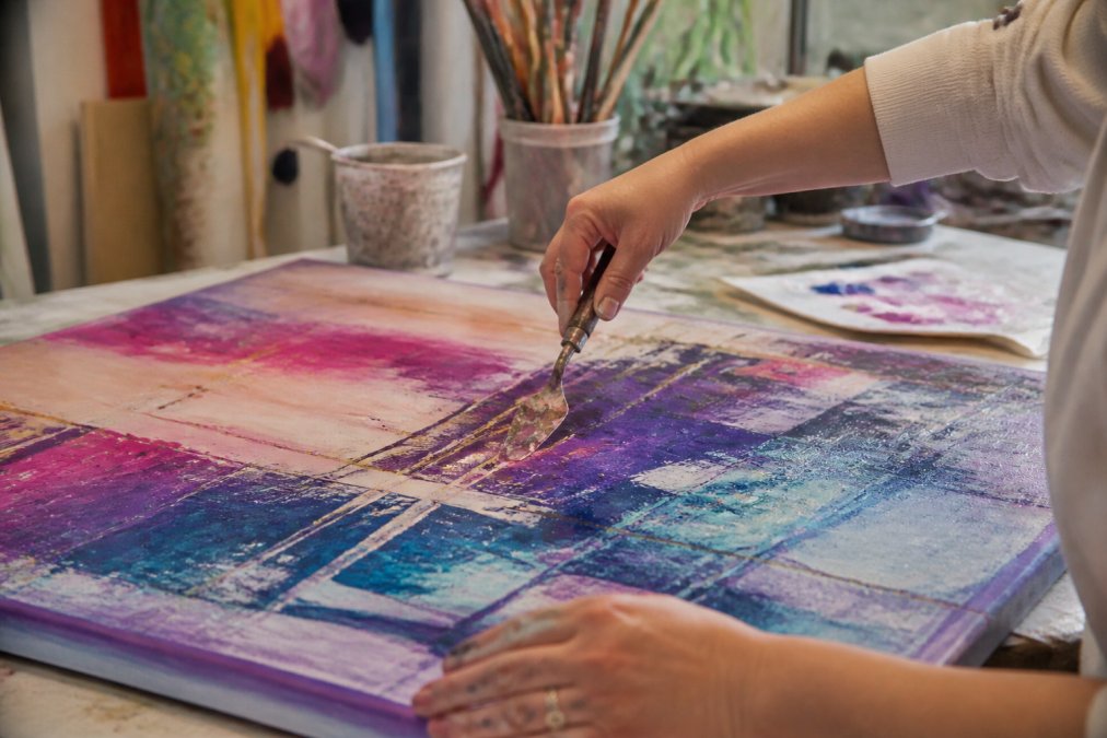 Hands working on an abstract memorial art piece with vibrant, emotional brushstrokes and layered colors conveying healing and remembrance