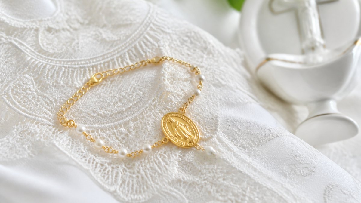 A close-up of a delicate gold-plated Miraculous Medal bracelet with pearl accents resting on a white lace baptism gown, soft natural light, a small holy water font blurred in the background