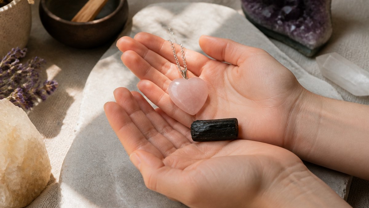 Hands holding a polished rose quartz heart pendant and a black tourmaline stone in soft natural light