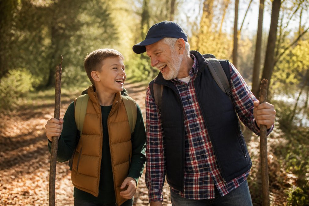 Grandparent and grandchild laughing together outdoors during nature walk in sunlit park, genuine connection and joy visible
