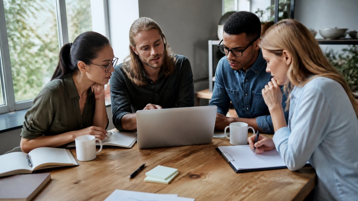 Small team of employees gathered around a wooden table reviewing survey results and engagement data on a laptop, with notebooks and coffee cups visible, natural office lighting from nearby windows