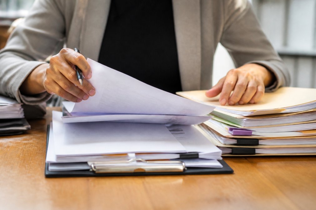 Close-up of hands organizing and reviewing medical documents, files, and records on table with clipboard and pen