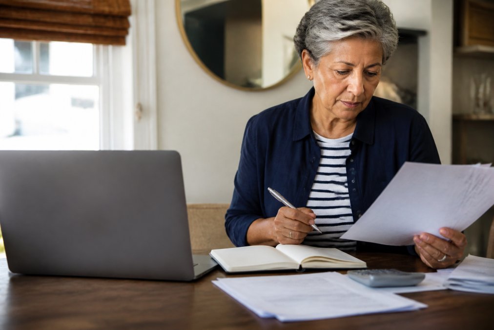 Senior adult reviewing Medicare plan documents at home with a laptop and notepad, looking focused and informed while making healthcare decisions