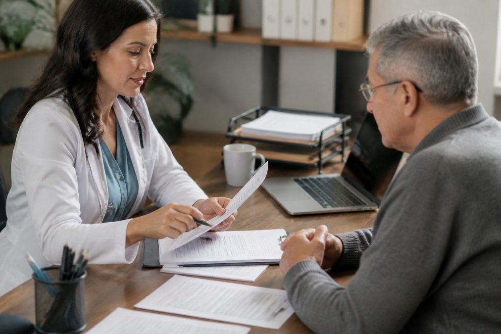 Healthcare provider reviewing Medicare enrollment documents with patient at desk with paperwork and computer visible