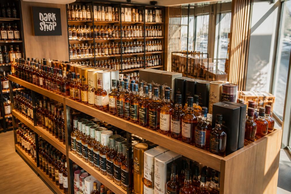 Półki z butelkami whisky single malt i blended whisky w nowoczesnym sklepie specjalistycznym, różne etykiety i kolory trunków widoczne z góry, drewniane regały oświetlone naturalnym światłem