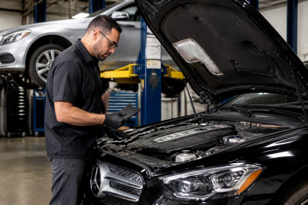 ASE-certified mechanic performing a Mercedes-Benz service using a diagnostic tablet in a modern auto shop