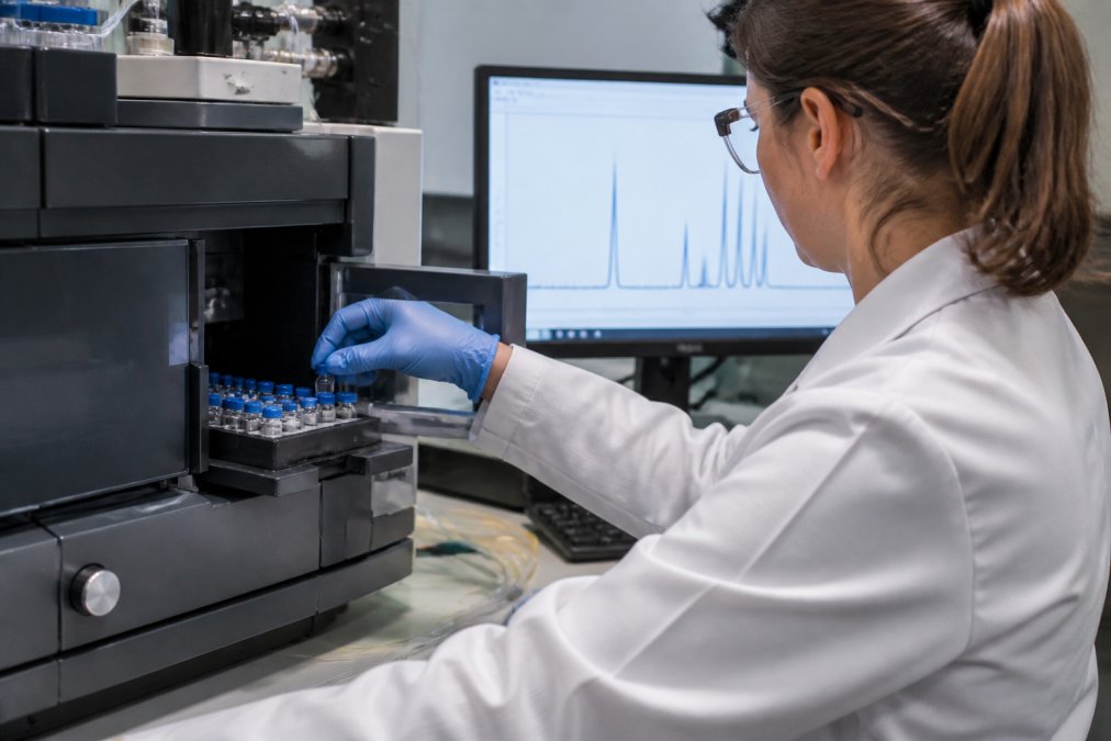 Researcher loading vials into an HPLC system to verify metabolic peptide study purity requirements via chromatograms.