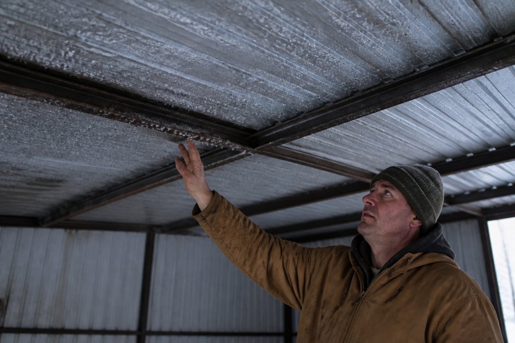 Farmer inspecting frost and condensation on steel barn panels needing metal building insulation