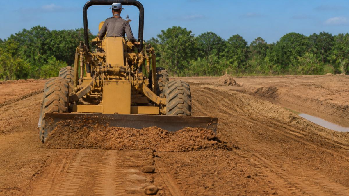 Heavy equipment operator grading land for metal building site prep with visible drainage channels