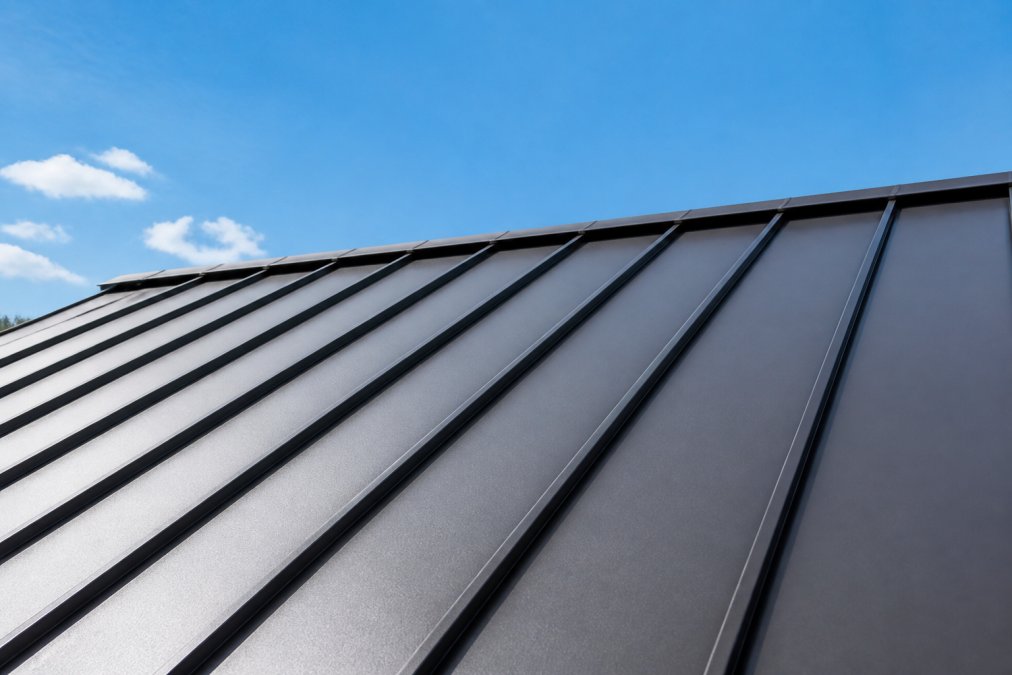 Close-up of standing seam metal roof panels showing interlocking seams and reflective surface with clear blue sky visible above the roofline