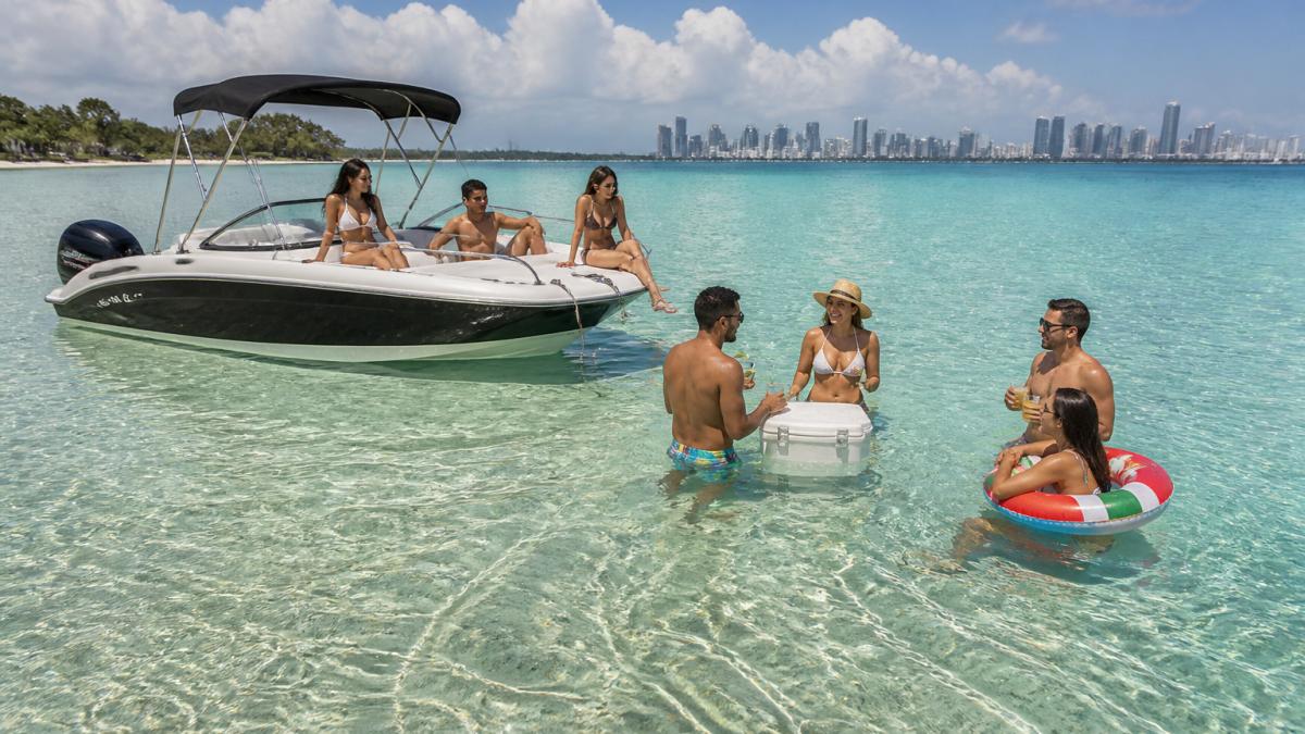 Friends enjoying a Miami boat rental at a shallow sandbar in Biscayne Bay with the city skyline in the background.