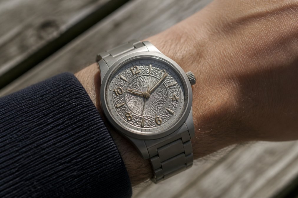 Hand-finished titanium microbrand watch on a wrist, showing ornate dial decoration with applied numerals and guilloche center work in natural daylight, highlighting case craftsmanship and dial detail