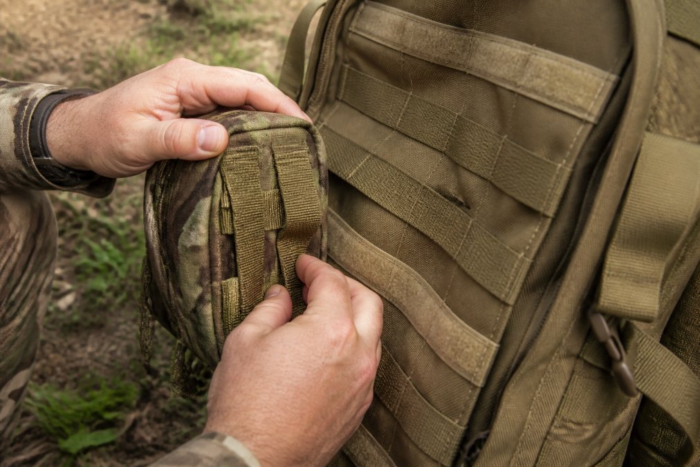 Step-by-step process of attaching a modular pouch to the MOLLE webbing grid on military backpacks.