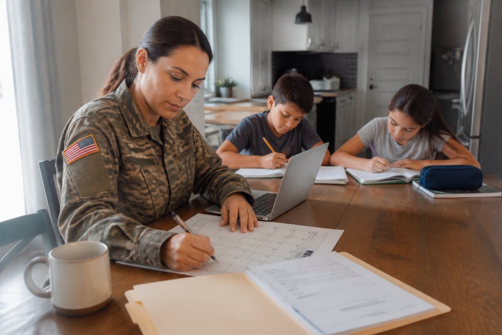 A service member plans a PCS timeline at the kitchen table while her children do homework.