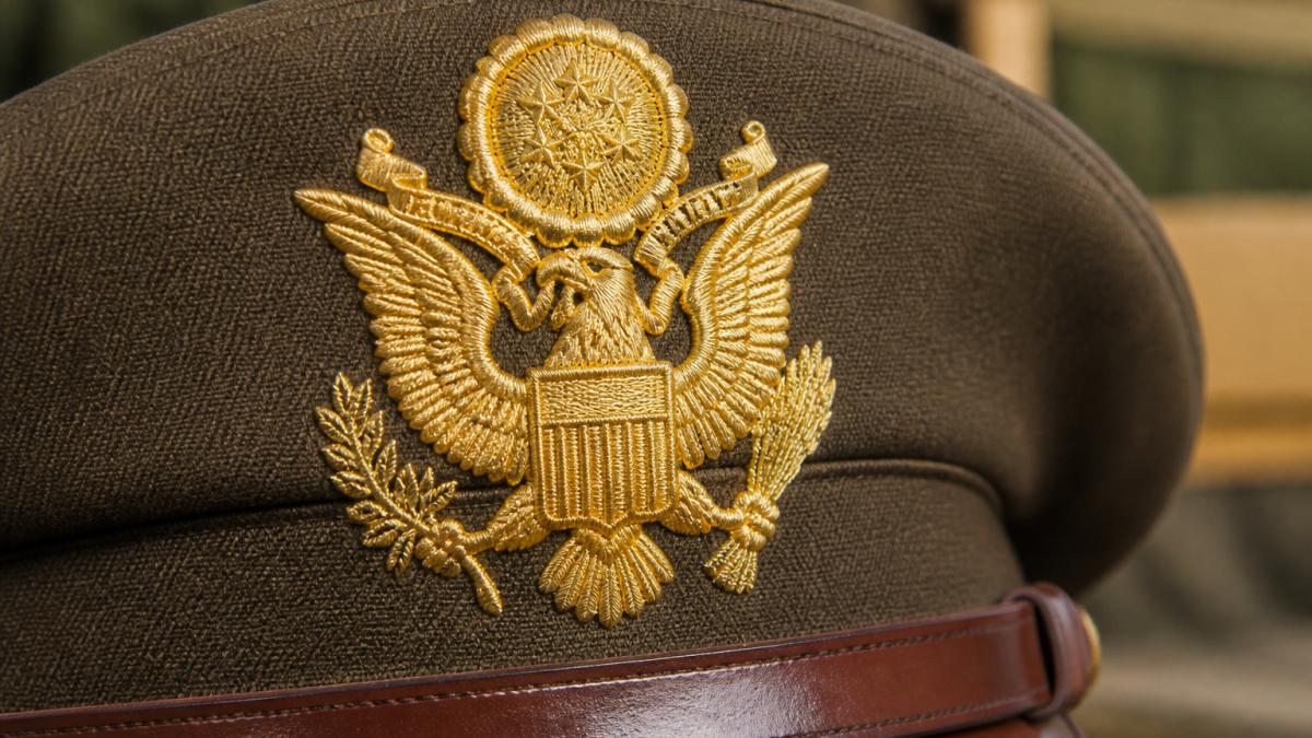 Close-up of embroidered military insignia on a peaked service cap showing detailed badge craftsmanship with gilt threading and uniform stitching