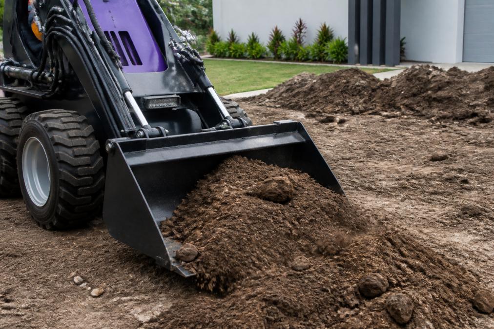 Infographic showing a Kanga mini loader using a 4-in-1 bucket to scoop soil, helping you estimate your mini loader hire cost.