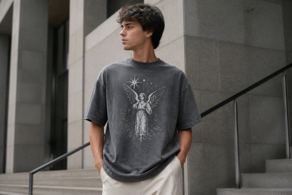 Young person wearing a vintage washed oversized celestial angel number tee, standing in an urban streetwear setting with neutral architecture, soft natural lighting catching the fabric texture