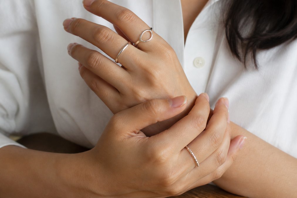 Close-up of hands wearing multiple delicate minimalist silver rings in everyday settings, showing different band widths and styles together on fingers