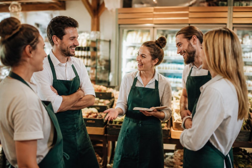 Lachendes Einzelhandelsteam bei einer Teambesprechung als Beispiel für positive Mitarbeiterbindung Einzelhandel Benefits.