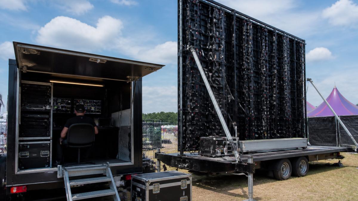 Professional LED screen mounted on mobile trailer at festival site with technical setup and control room visible in daylight