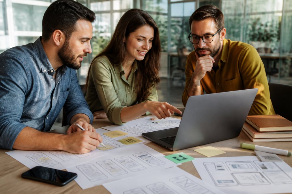 Small business owner reviewing wireframes with a mobile app development for small business partner in a bright office.