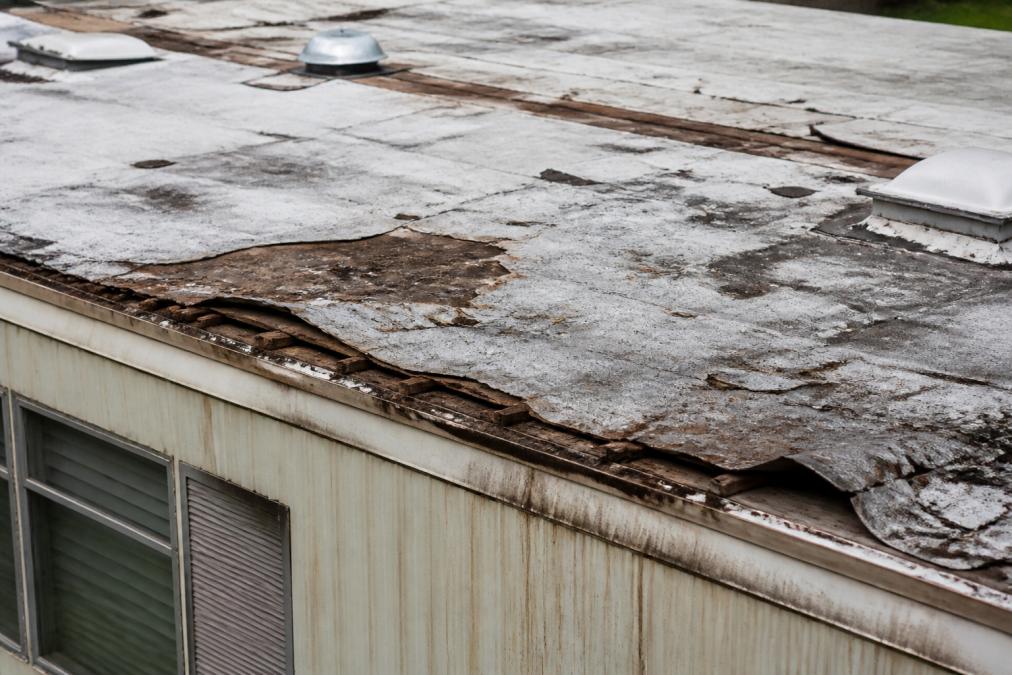 Close-up of deteriorated mobile home roof showing soft spots, water-damaged shingles, rust staining, and visible gaps where moisture has entered