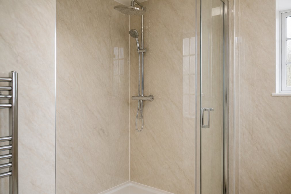 Modern bathroom with beige marble wall panels installed around a shower enclosure, showing seamless waterproof finish, soft natural lighting reflecting off the stone-effect surface, and contemporary chrome fixtures