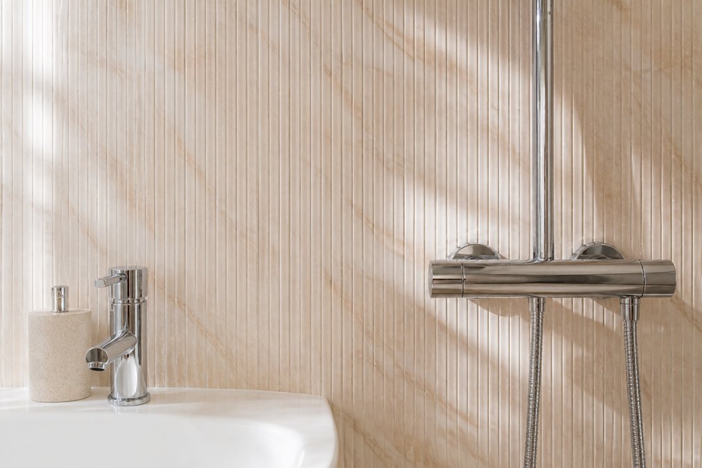 Close-up of modern textured slatwall bathroom panels showing grooved finish with light reflection creating subtle shadow patterns, installed in contemporary bathroom setting with chrome fixtures visible