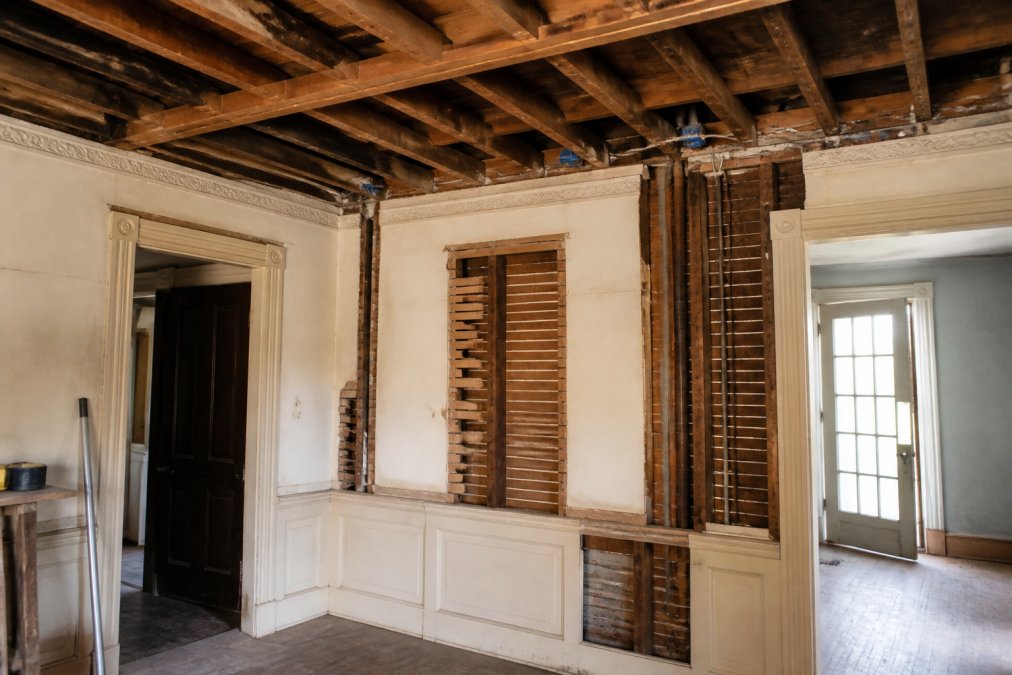 Interior view of a historic home showing exposed wooden ceiling beams, original plaster walls with ornate trim, and visible structural challenges where modern ductwork would need to be routed through limited wall cavities