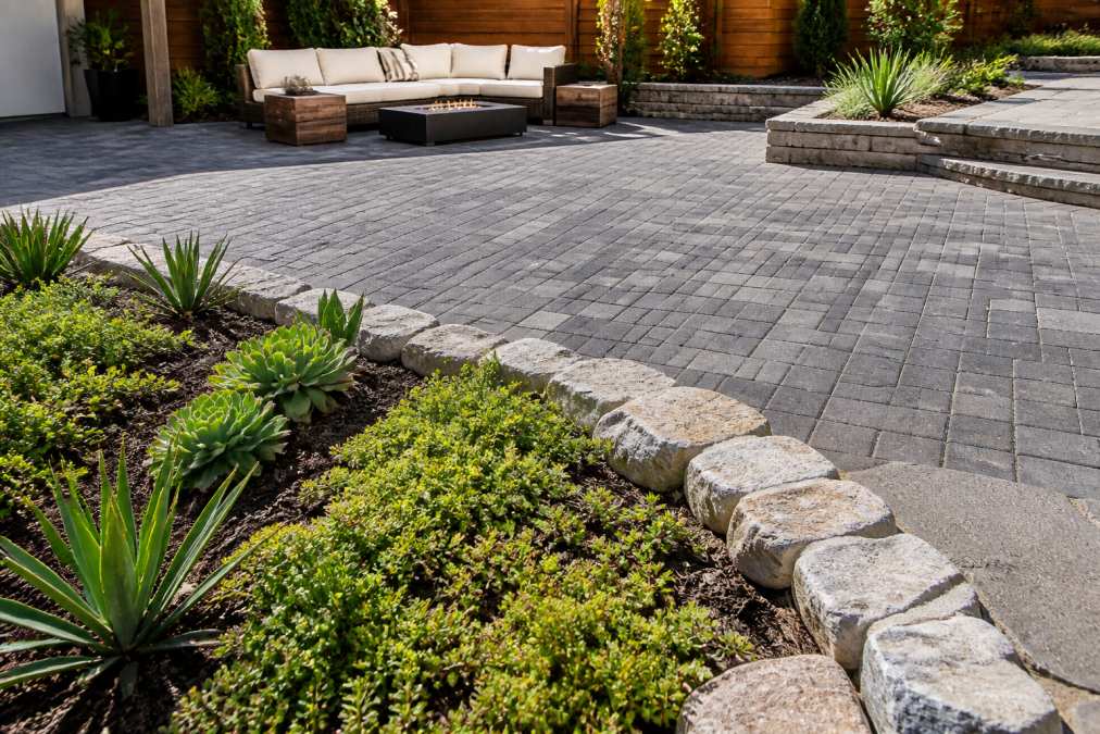 Close-up of a beautifully laid permeable paver patio with natural stone edging, surrounded by drought-tolerant ground cover plants in a contemporary backyard setting