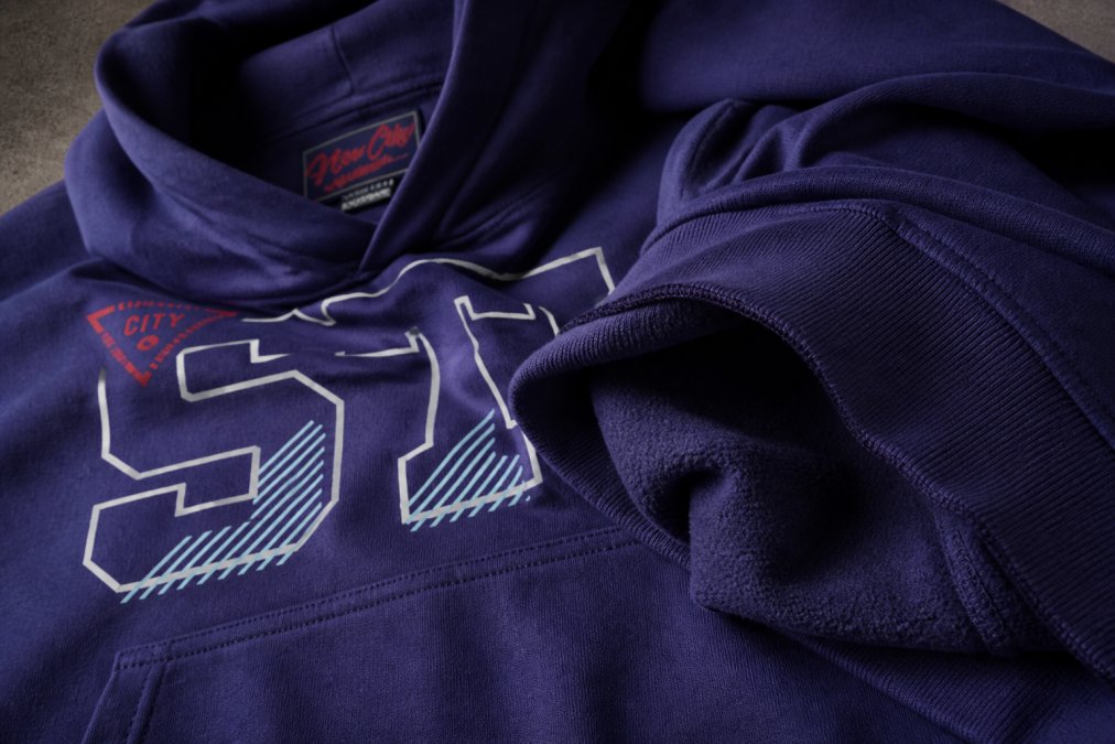 Close-up detail shot of premium fabric textures: snow-washed cotton with natural fading, brushed fleece interior with visible texture, and raw seams on a quality streetwear piece, demonstrating craftsmanship and material quality under warm studio lighting