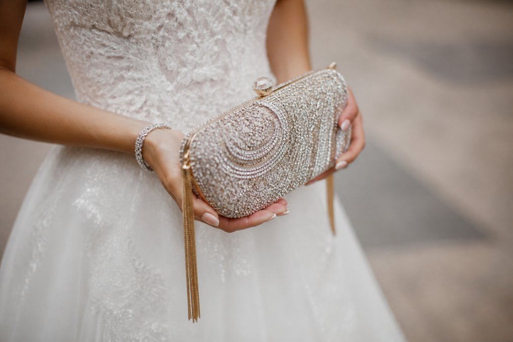 Close-up of a crystal-embellished clutch bag with delicate tassels held by a bride in her wedding dress, showing sparkle and detail in natural lighting