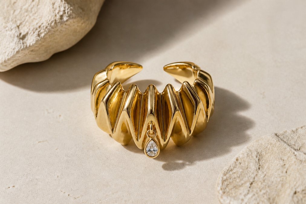 Close-up of geometric modernist jewelry pieces displayed on a neutral cream surface, showing sculptural forms with clean architectural lines, mixed metals catching soft natural light, and faceted gemstones arranged to emphasize angular planes and minimalist aesthetic