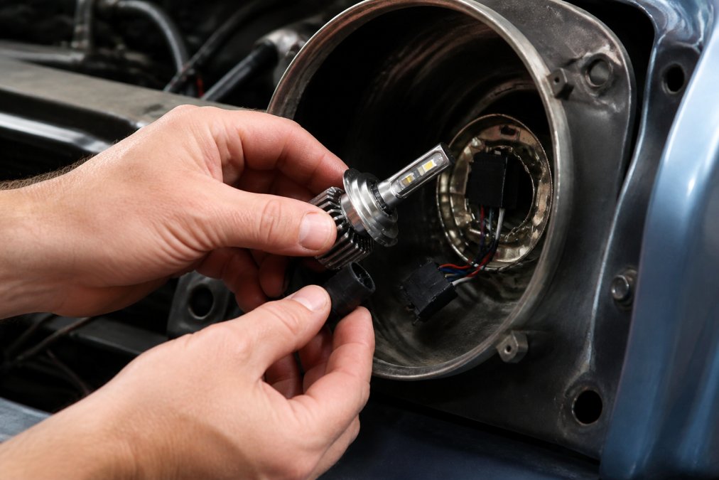 A person's hands installing a plug-and-play LED headlight bulb into an older car's headlight housing, with the wiring harness clearly visible and no tools nearby