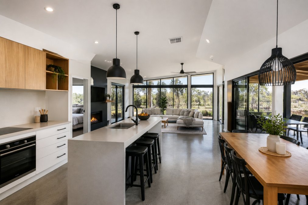 Interior of a custom modular home showing an open-plan living area with polished concrete floors, high-quality cabinetry, large north-facing windows flooding the space with natural light, and contemporary pendant lighting