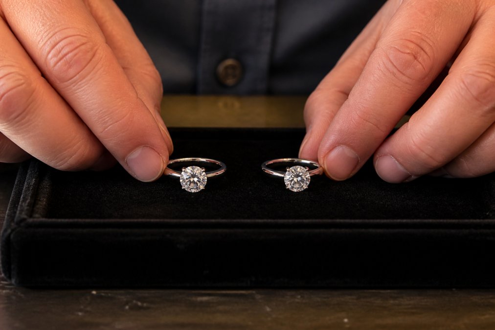 Jeweler holding a moissanite and a diamond wedding band side by side on a dark velvet tray