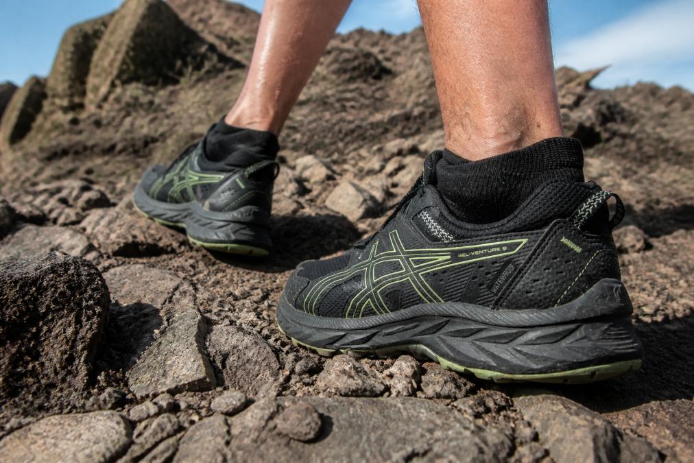 Trail runner's feet in moisture-wicking socks navigating rocky, debris-filled mountain terrain during an intense trail run, showing the socks in action against jagged rock and dirt