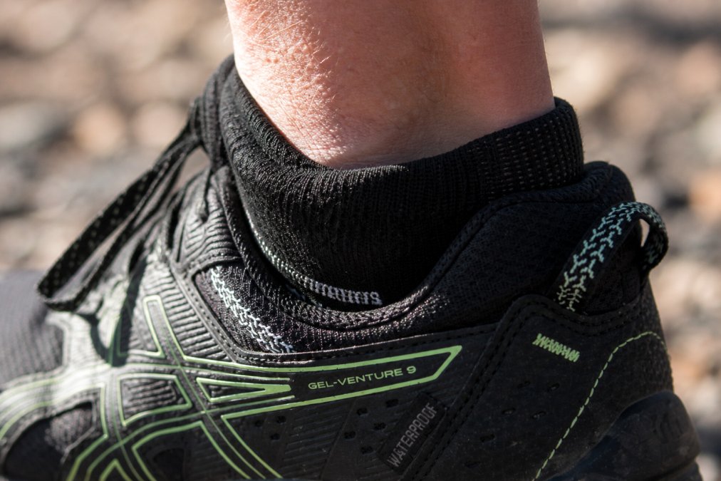 Close-up detail of a sock's polyurethane debris-blocking cuff design at the shoe collar, showing the protective barrier that prevents dirt and gravel from entering the shoe