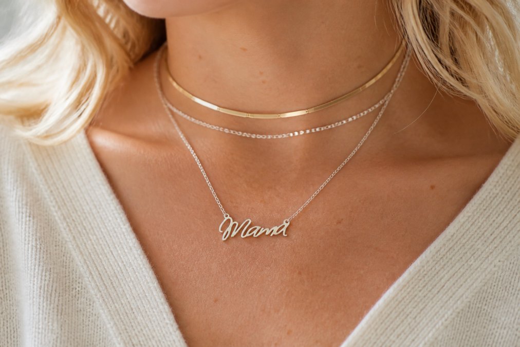 Close-up of a delicate sterling silver mama necklace displayed on a woman's chest, showing the pendant detail and how it layers with other jewelry pieces